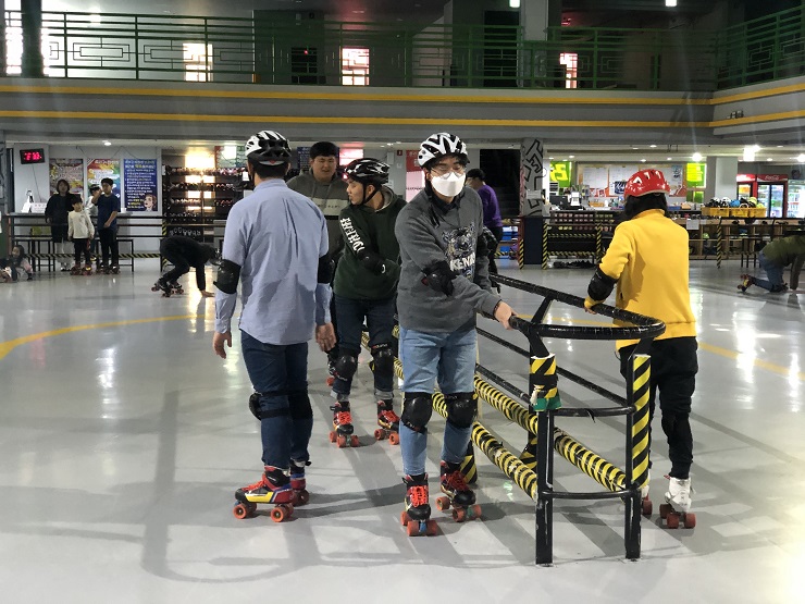 롤러스케이트 장 가운데 있는 기둥을 잡고 롤러스케이트를 연습하고 있는 모습