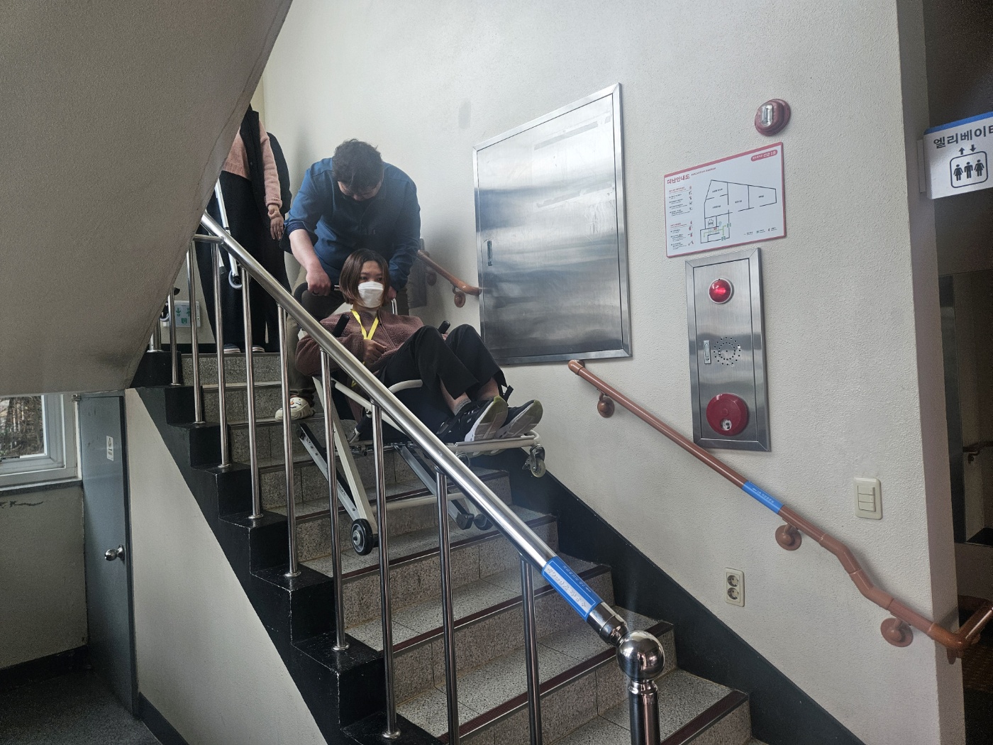 긴급 비상용 계단이동 기구를 타고 내려오는 이용인과 이동을 지원하는 직원의 모습입니다. 