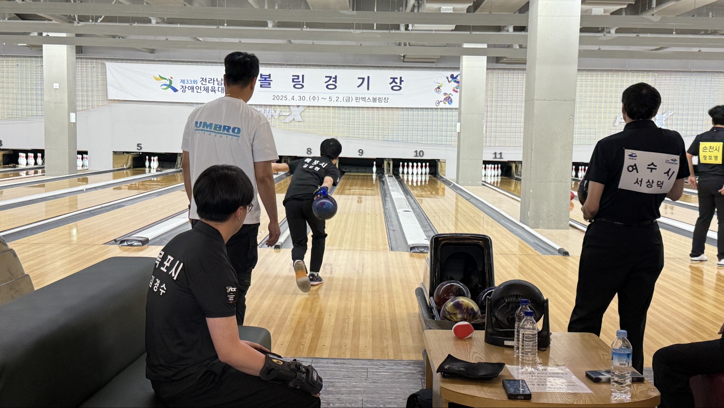 볼링경기장에서 경기를 참여하고 있는 선수들과 선수들의 뒤에서 지켜보고 있는 담당교사의 뒷모습 사진입니다.