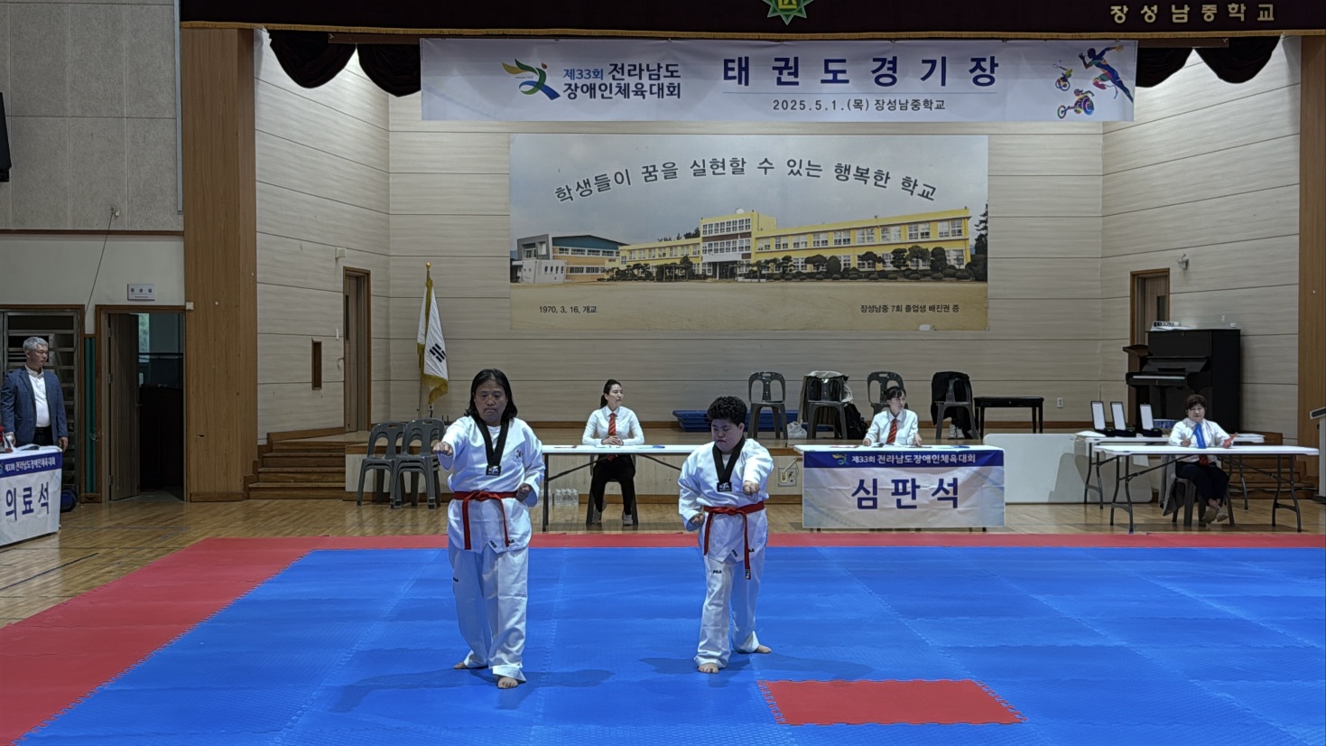 태권도경기장에서 품새를 넣으며 경기에 참여하고 있는 두 여자 이용인의 모습입니다.