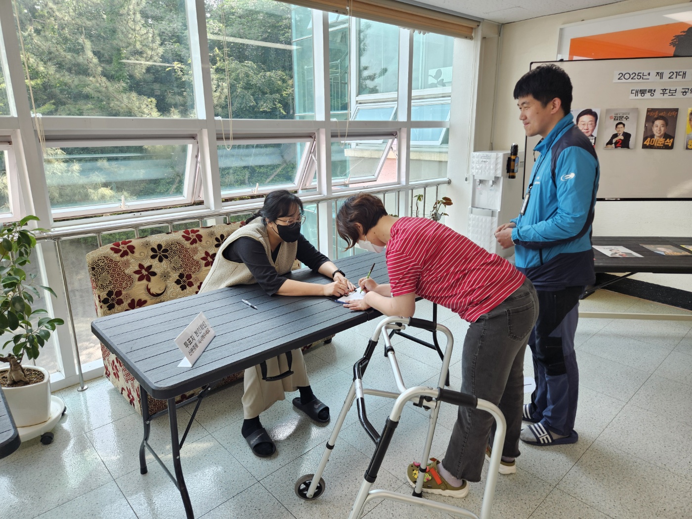 신분증을 제시한 뒤, 본인확인을 하고 본인확인 대장에 서명을 하고 있는 이용인의 모습과 그 뒤에서 대기를 하고 있는 이용인의 모습입니다. 
