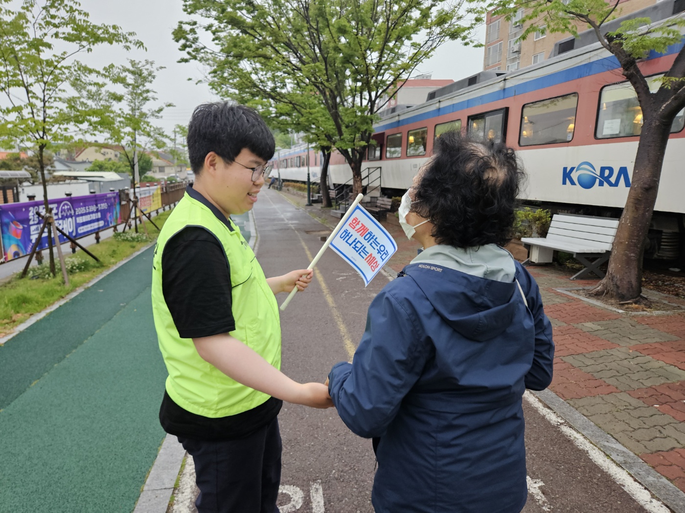 함께하는 우리, 하나되는 세상이라는 깃발을 든 장애당사자와 이웃주민이 함께 손을 잡고 이야기를 나누는 모습의 사진입니다. 