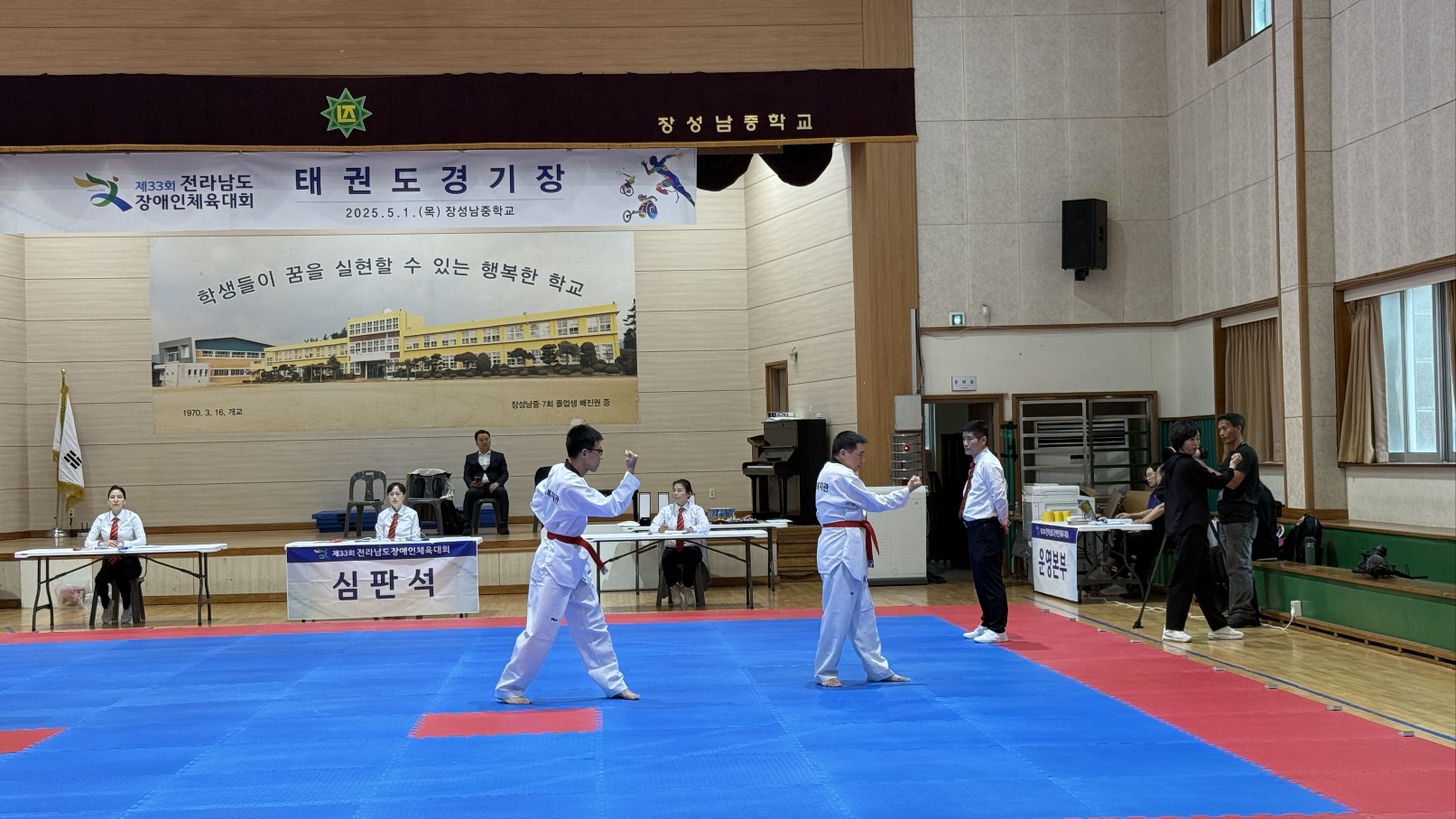 태권도경기장에서 품새를 넣으며 경기에 참여하고 있는 두 남자 이용인의 모습입니다.