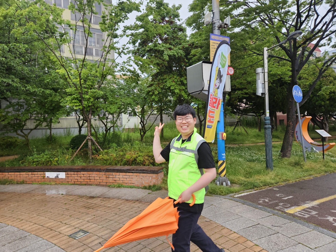 '달려라명도' 워킹배너를 매고 주황색 우산을 든 채, 밝게 웃으며 걷고 있는 장애당사자 모습의 사진입니다. 