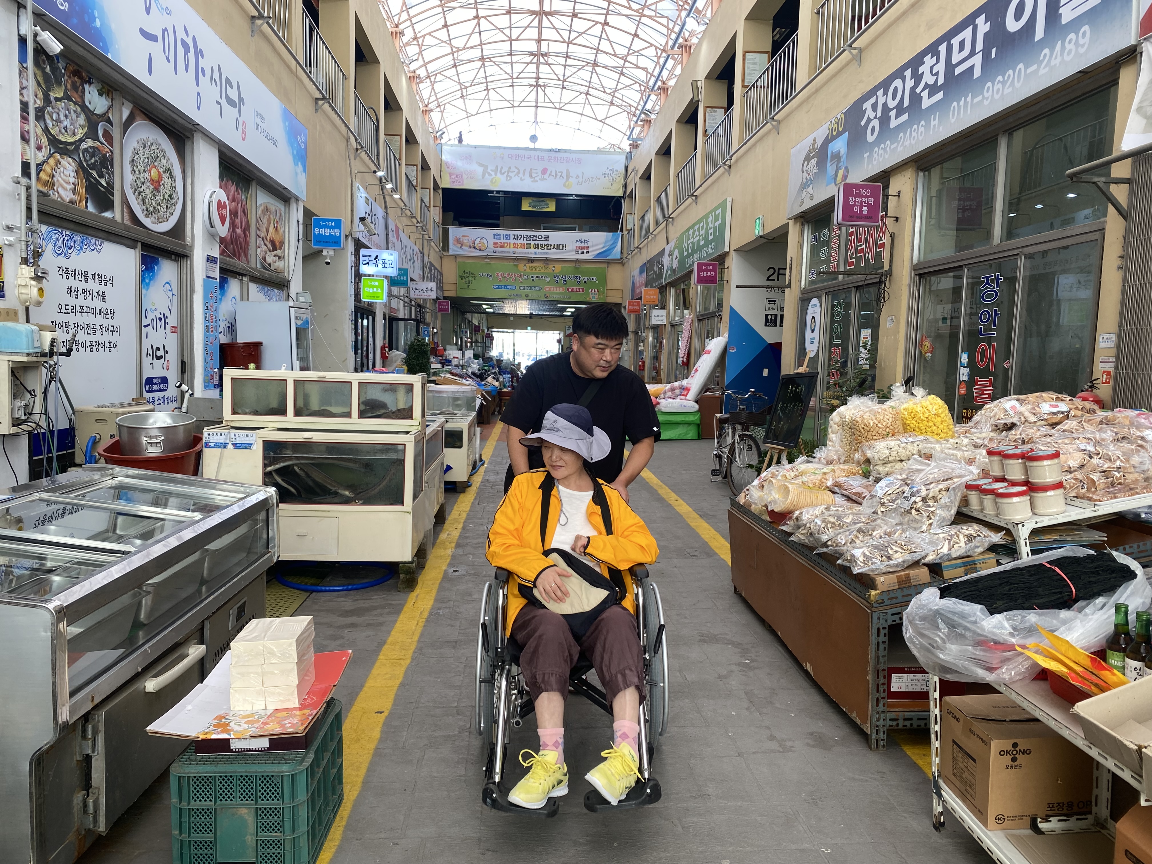 휠체어에 탄 이용인과 담당사회복지사가 시장을 구경하고 있는 모습입니다.