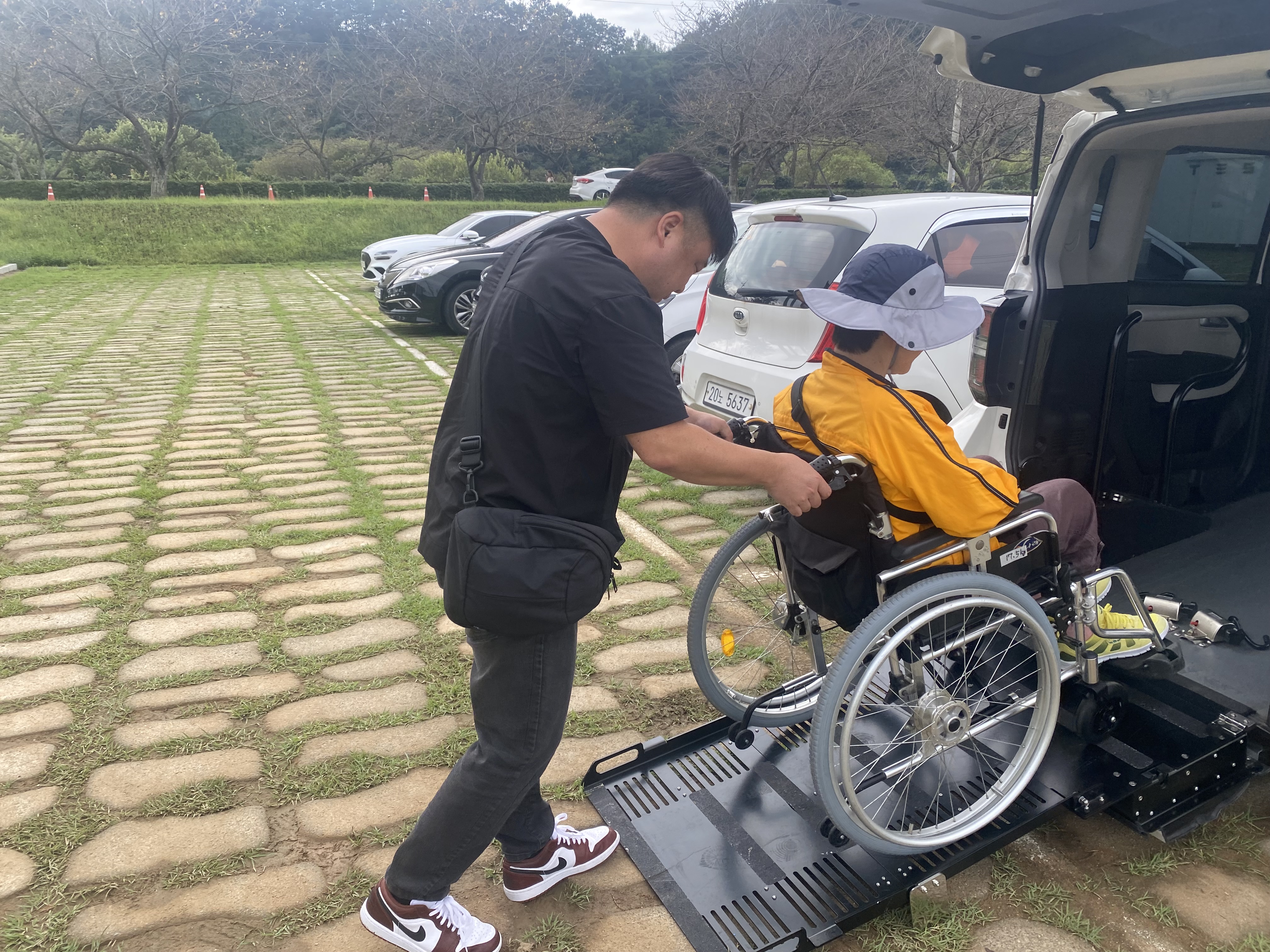 휠체어에 탄 이용인을 리프트카에 태워드리고 있는 사회복지사의 모습입니다.