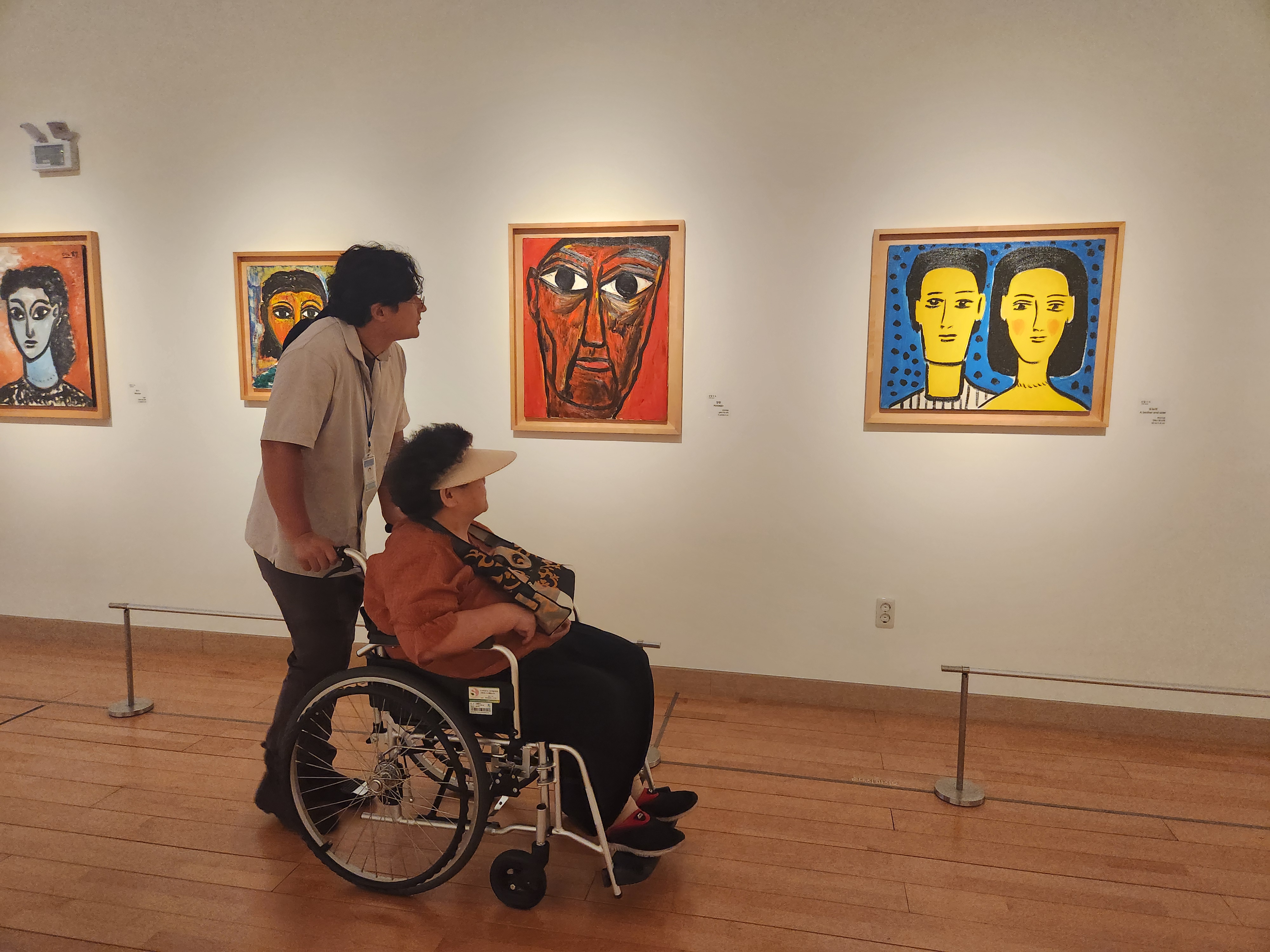 휠체어에 탄 이용인 담당 사회복지사가 함께 트로트가요센터를 관람하고 있는 모습입니다.