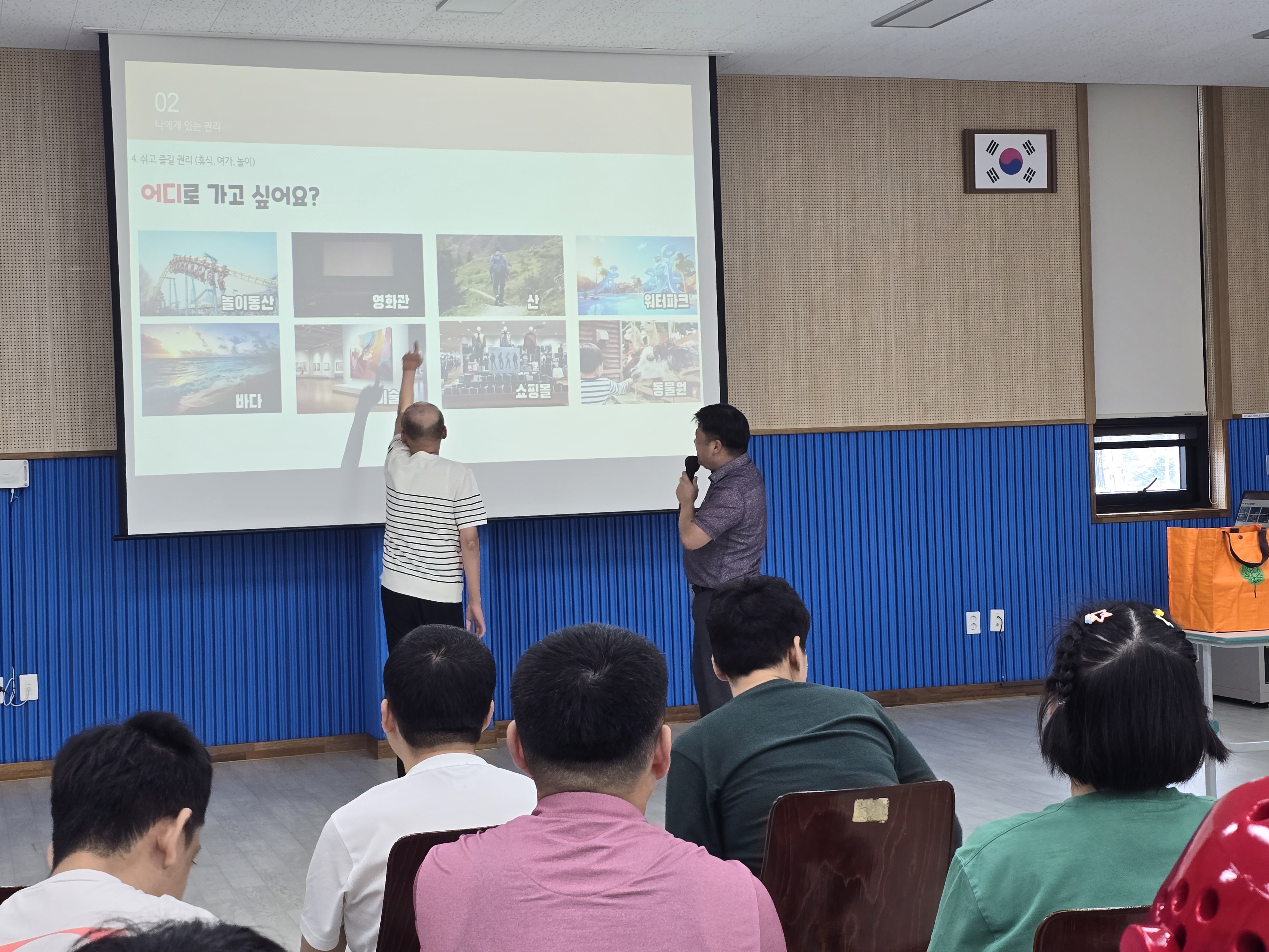 한 이용인이 앞으로 나와 화면 속 가고 싶은 장소를 손가락으로 가리키고 있는 모습입니다.