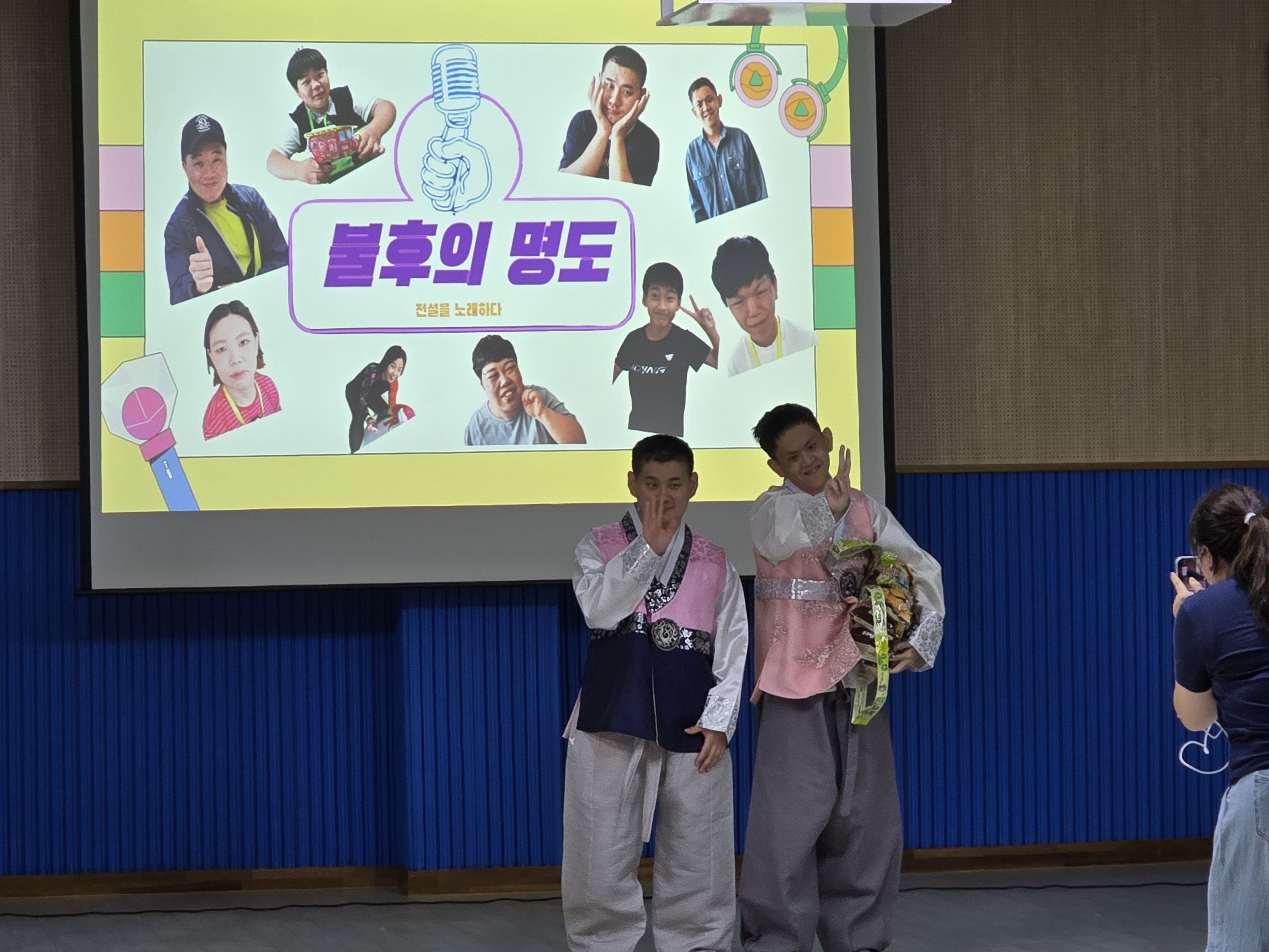 노래자랑행사에 참여하여 인기상을 수상한 남성 이용인 2명이 상품을 받고 사진을 찍으려 포즈를 취하고 있는 사진입니다.