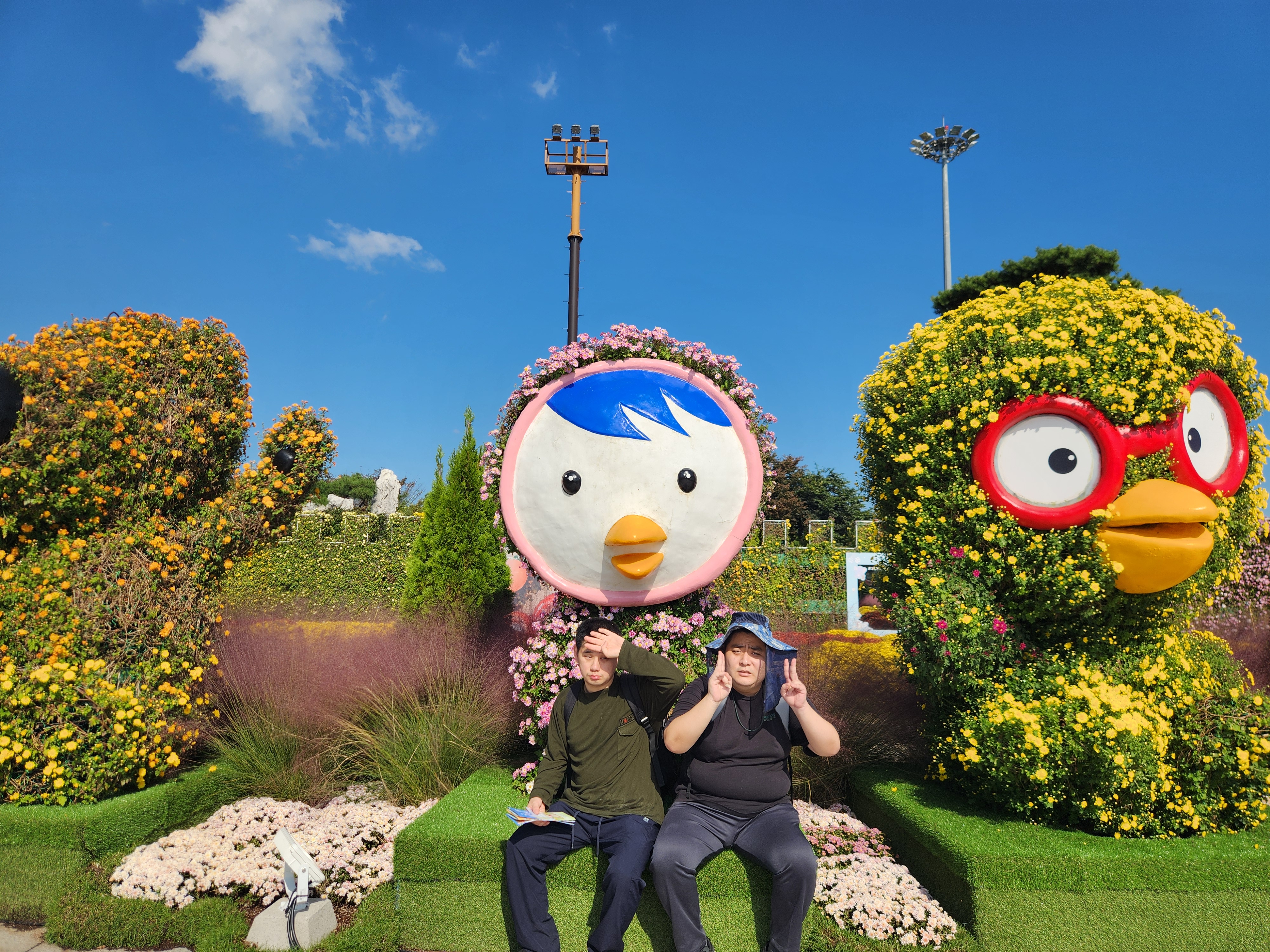 유명한 아동만화에 나오는 뽀로로 캐릭터 조형물 앞에 남성 이용인 2명이 앉아 포즈를 취하고 있는 모습입니다.