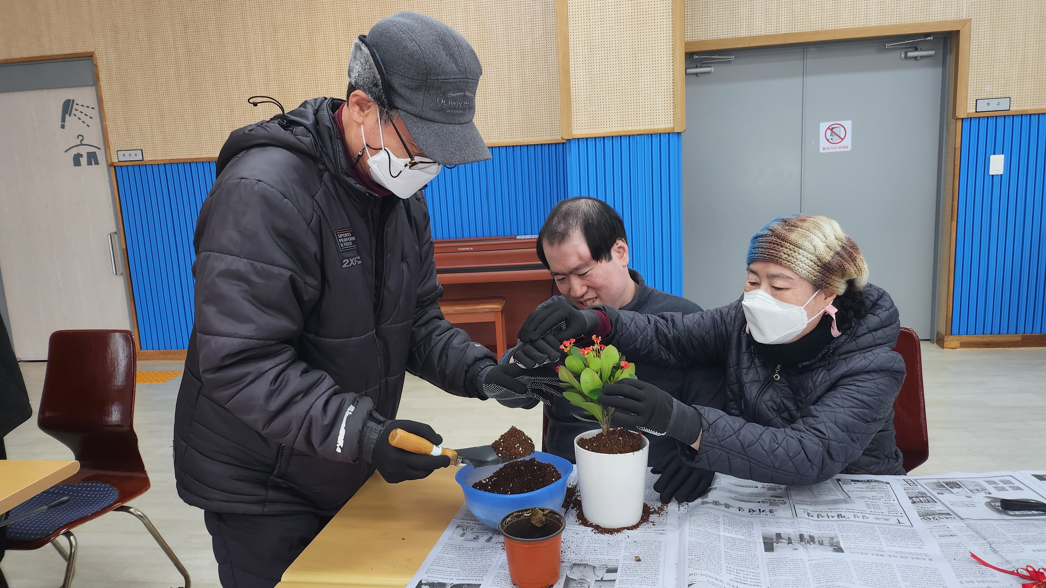 주간보호센터 이용인과 부모님이 함께 참여하여 화분에 흙을 담고 있는 사진입니다.